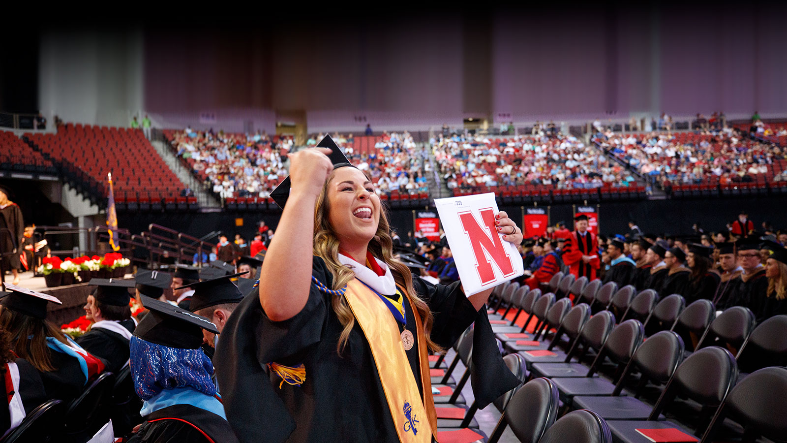 student in cap and gown holding up degree