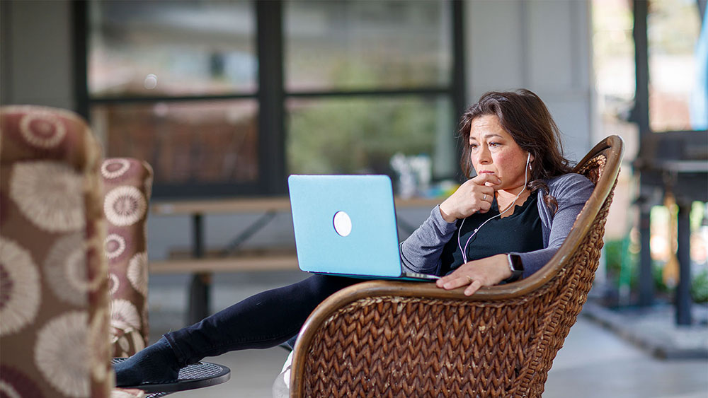 Person on laptop in chair in sunroom