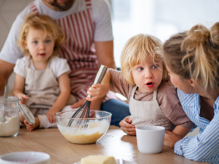 Three children cooking with an adult, mixing up batter in bowls