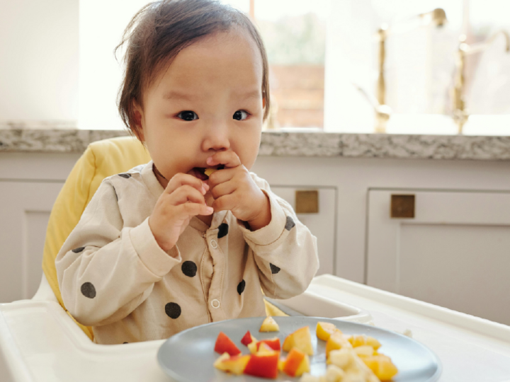 Young child eating fruits and vegetables in a high chair