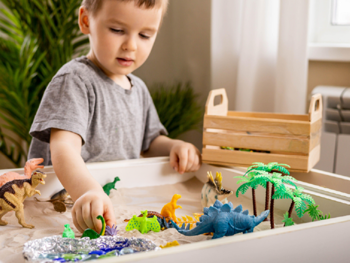 Young child playing with dinosaurs in a sandbox
