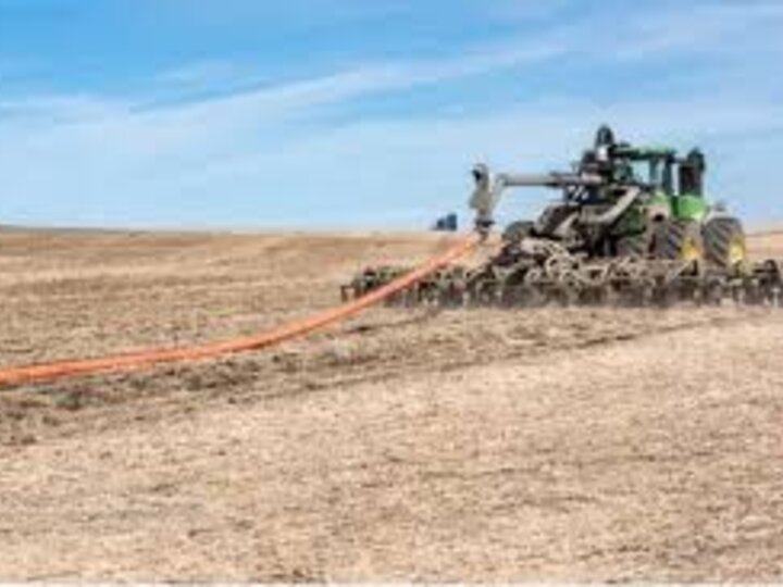Tractor pulling farming equipment across a dry, open field under a blue sky.