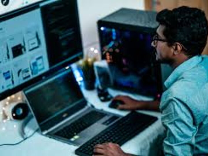 Person working at a desk with a laptop, monitor, keyboard, and computer tower in a home office.