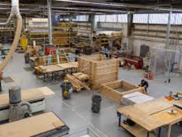 Large woodworking workshop with tables, tools, wooden structures, and industrial equipment.
